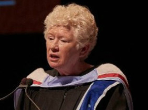 A woman in graduation gown speaking at an event.